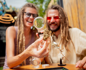 Hippie style couple examines under a magnifying glass the joints and buds of medical marijuana