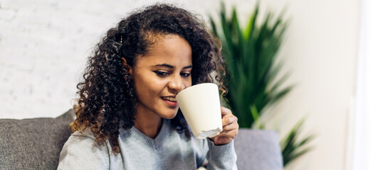 Portrait of smiling happy enjoy african woman relax drinking cup of hot coffee or tea,Cappuccino,Espresso,Americano,Latte.Girl felling enjoy breakfast in holiday morning vacation on bed at home