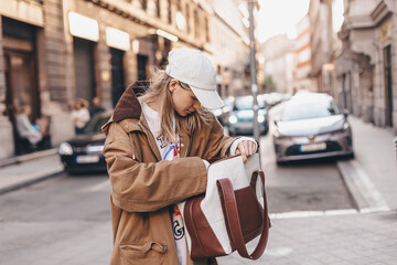 Elegant young woman looking in her brown and white bag her phone or purse. Traveler style woman...