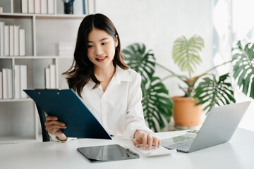 Fototapeta premium Confident Asian woman with a smile standing holding notepad and tablet at the modern office.