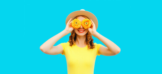 Plakat Summer portrait of happy smiling young woman covering her eyes with flowers as binoculars looking for something wearing round straw hat on blue background