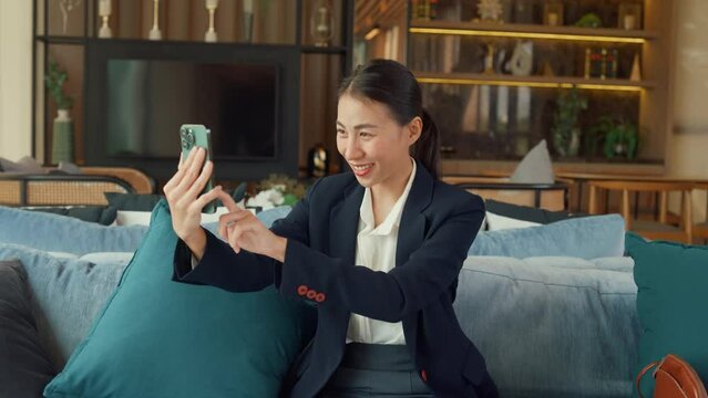 Youth Asia business female passenger wear suit sit on couch chair video call phone show luxury life social media in modern airline lounge wait for transit at airport. Travel business trip concept.