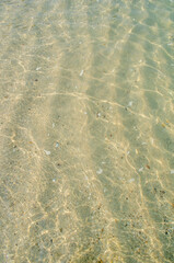 Background, wallpaper. Texture of sea sand through a layer of water with sun glare on the waves