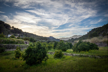 Fototapeta premium Panoramic view of the beautiful Valley of Guadalest, Alicante, at sunset with the sky with beautiful clouds and lemon groves surrounded by mountains