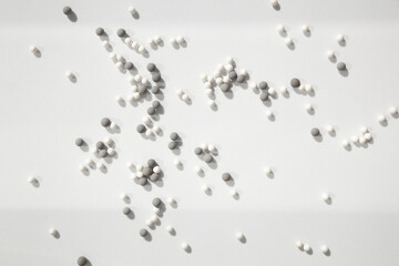 Many little white and gray balls scattered on a white background in the bright light, dropping...