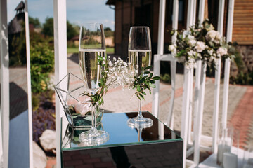 Fototapeta na wymiar Stylish modern wedding arch with fresh flowers and a table with glasses of champagne for the newlyweds, in the park. Creative image for your design or illustrations.