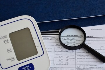 A health insurance document on a table with a blood pressure monitor, a folder, and a magnifying...
