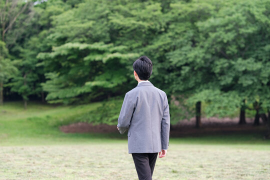 新緑の公園を歩くビジネスマンの後ろ姿