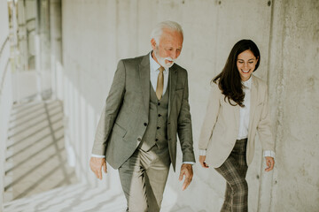 Senior corporate business professional and his young female colleague climbing at stairs in office corridor