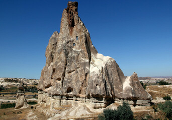 Fototapeta na wymiar A huge iceberg-shaped mountain with many caves inside against a bright blue sky in the Rose Valley between the towns of Goreme and Cavusin in Cappadocia, Turkey
