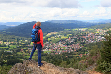 Male hiker (man) standing on mountain Silberberg and looking at panorama of municipality Bodenmais in Bavarian Forest, Germany