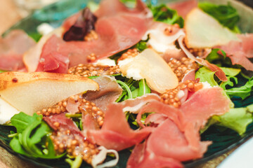 Salad with herbs, arugula, prosciutto, cheese, green olives and nuts.