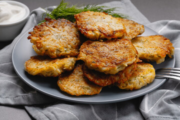 Close up view of potato pancakes. Potatoes pancakes latkes, flapjacks, hashbrown or potato vada on gray plate over gray wooden table, with fresh dill and sour cream