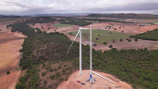 Elevated view of a wind turbine with a group of workers installing a blade on the nacelle in a wind farm under construction. Team of professional with a giant crane lifting a blade. Renewable, Spain