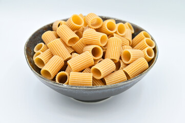 Whole wheat mezze Rigatoni pasta, in a dark grey bowl, isolated on a white background
