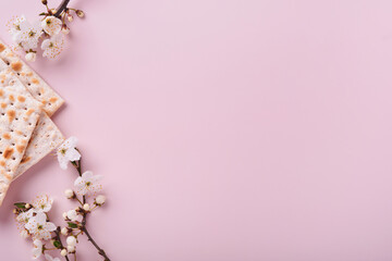 Passover celebration concept. Matzah, red kosher wine, walnut and spring beautiful branch of full bloom cherry or apple. Traditional Jewish bread on light pink background.  Pesach Jewish holiday.