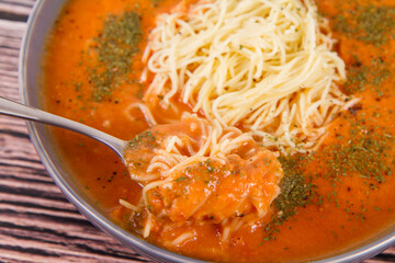 Tomato soup with noodles being eaten with spoon on a wooden background	