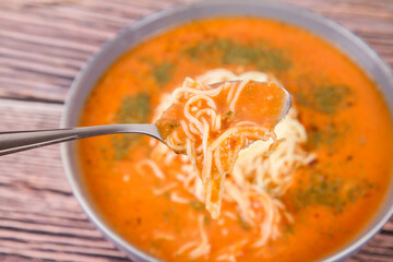 Tomato soup with noodles being eaten with spoon on a wooden background	