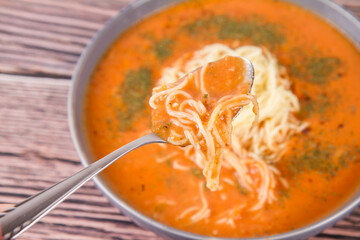 Tomato soup with noodles being eaten with spoon on a wooden background	