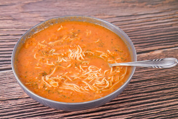 Tomato soup with noodles being eaten with spoon on a wooden background	