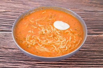 Tomato soup with noodles and a spoonful of cream on a wooden background