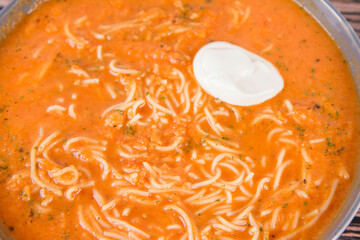 Tomato soup with noodles and a spoonful of cream on a wooden background