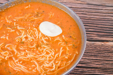 Tomato soup with noodles and a spoonful of cream on a wooden background