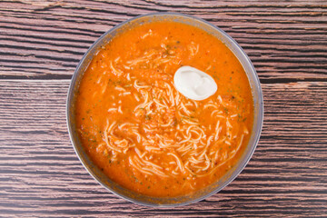 Tomato soup with noodles and a spoonful of cream on a wooden background