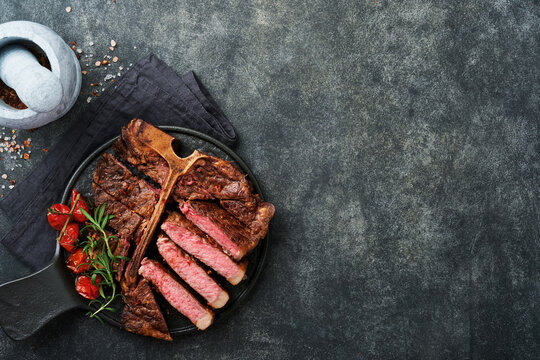 Steaks T-bone. Sliced beef grilled T-bone or porterhouse meat steak with spices rosemary and pepper on black marble board on old wooden background. Top view. Mock up.