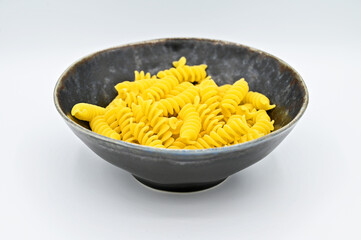 Fussili pasta in a dark grey bowl, isolated on a white background