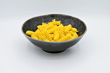 Fussili pasta in a dark grey bowl, isolated on a white background