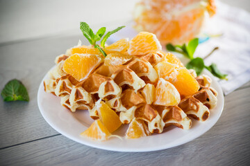 Cooked sweet Belgian waffles with oranges on the table.