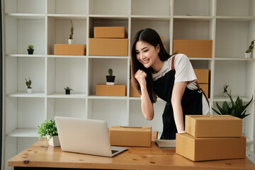Startup SME small business entrepreneur of freelance Asian woman using a laptop with box Cheerful success happy Asian woman her hand lifts up online marketing packaging and delivery SME idea concept