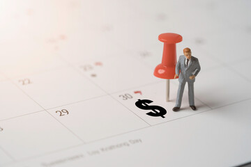 Businessman figure and red pin with dollar sign on calendar for plan and appointment of employee  salary payment concept.