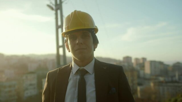 A Young, Handsome, Suit-and-Tie-Clad, Beardless, Helmeted Businessman or Urban Planner Smiling at the Camera with a Cityscape Background