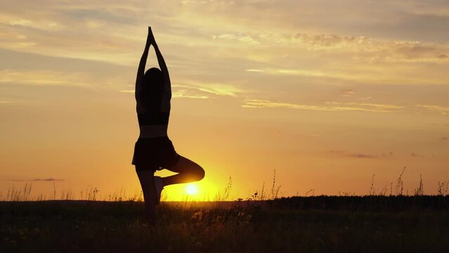 Silhouette Woman practicing yoga pose for meditation in summer on vacation, happy relaxed girl. Calm female exercises with yoga meditate on meadow against sun with sunset time. Mental physical health