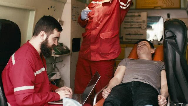 life saving concept. A professional paramedic uses a laptop to complete an injured patient's questionnaire on the way to the hospital. A paramedic works in an ambulance