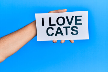 Hand of caucasian man holding paper with i love cats message over isolated blue background