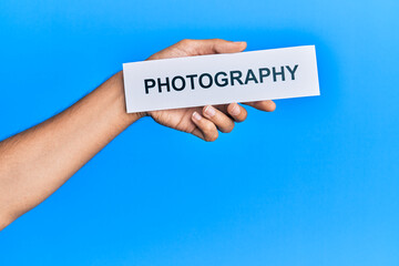 Hand of caucasian man holding paper with photography word over isolated blue background