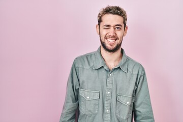 Hispanic man with beard standing over pink background winking looking at the camera with sexy expression, cheerful and happy face.