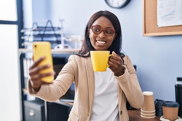 Young african american woman business worker make selfie by the smartphone drinking coffee at office