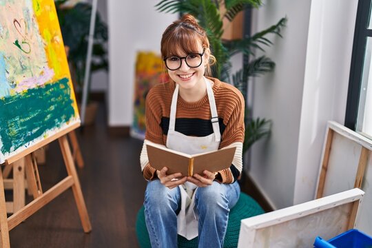 Young woman artist smiling confident reading book at art studio