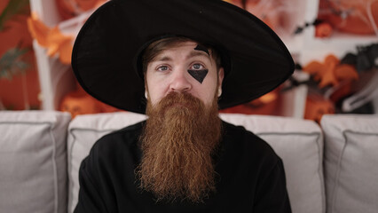 Young redhead man wearing wizard costume having halloween party at home