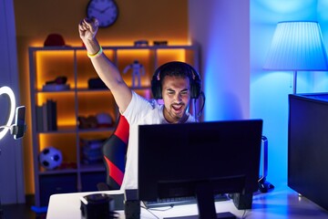 Young hispanic man streamer playing video game with winner expression at gaming room