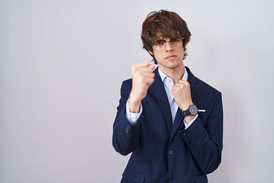Hispanic business young man wearing glasses ready to fight with fist defense gesture, angry and upset face, afraid of problem