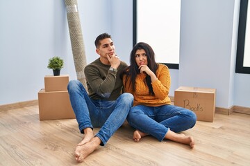Obraz premium Young couple sitting on the floor at new home thinking worried about a question, concerned and nervous with hand on chin