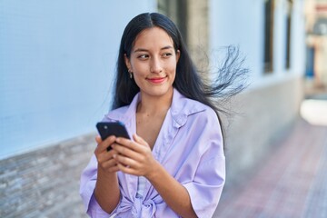 Young beautiful hispanic woman smiling confident using smartphone at street