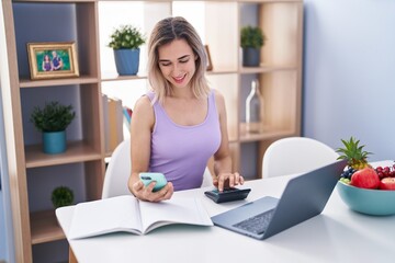 Young woman using smartphone and calculator studying at home