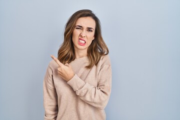 Young woman standing over isolated background pointing aside worried and nervous with forefinger,...