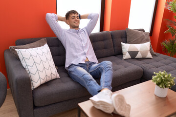Young hispanic man relaxed with hands on head sitting on sofa at home
